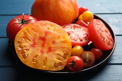 Photo of Different ripe tomatoes on blue wooden table, closeup