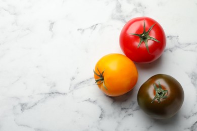 Photo of Different ripe tomatoes on white marble table, flat lay. Space for text