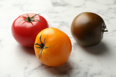 Photo of Different ripe tomatoes on white marble table, closeup