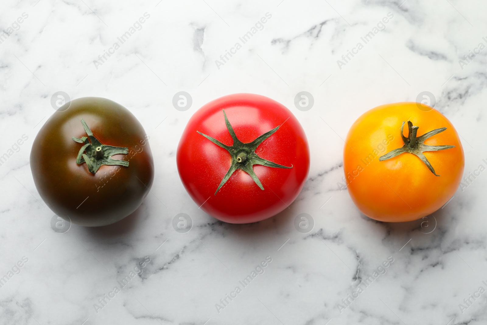 Photo of Different ripe tomatoes on white marble table, flat lay