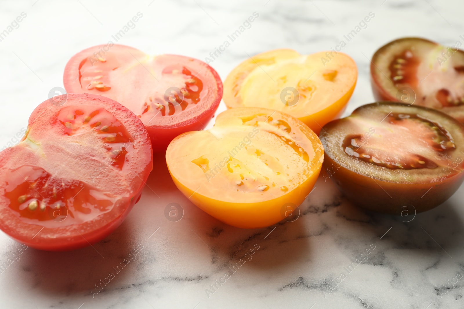 Photo of Pieces of different ripe tomatoes on white marble table, closeup