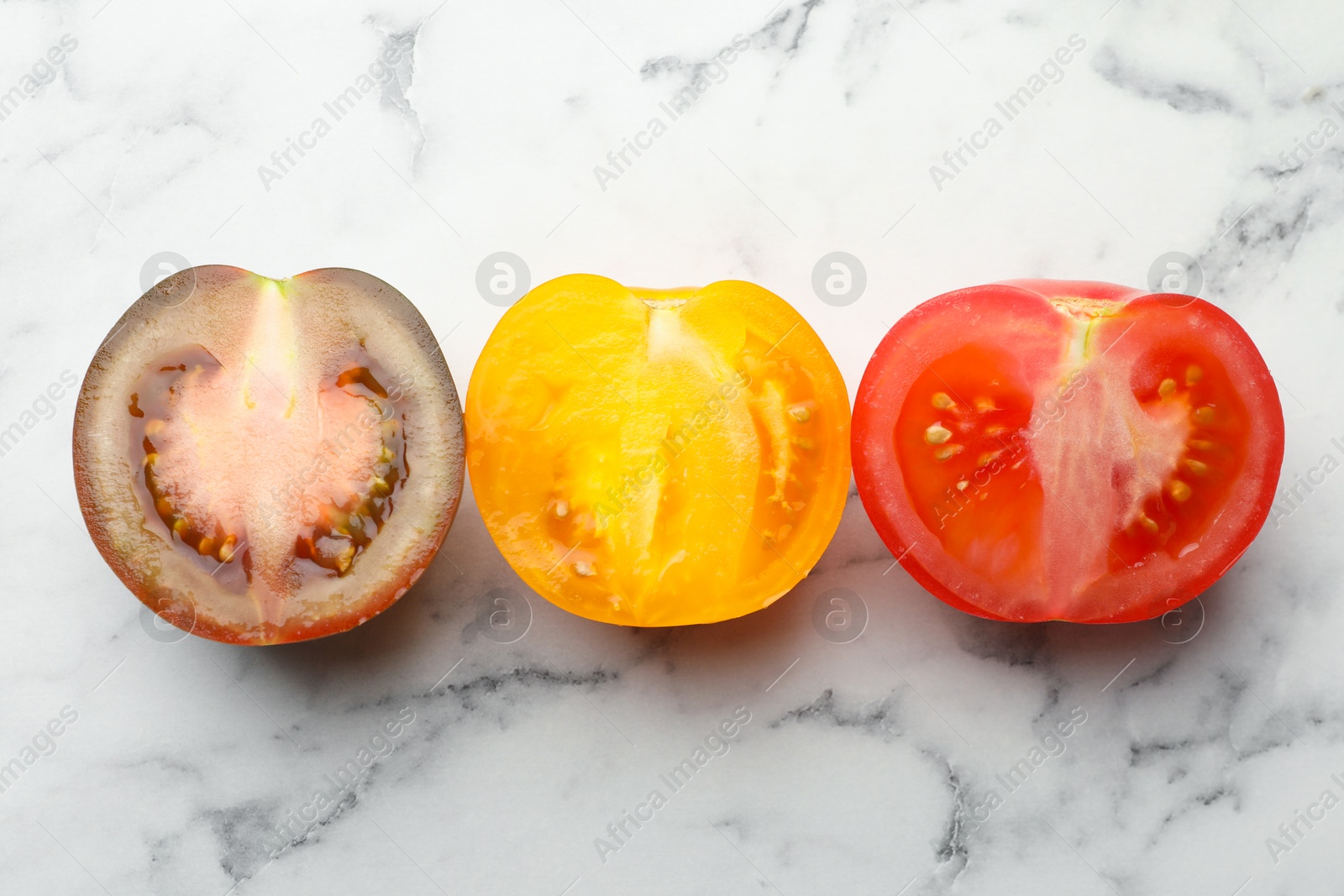 Photo of Pieces of different ripe tomatoes on white marble table, flat lay