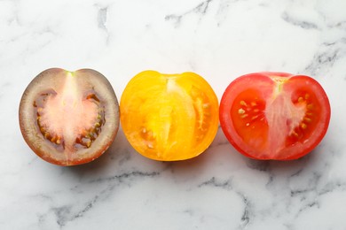Photo of Pieces of different ripe tomatoes on white marble table, flat lay