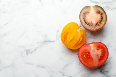 Photo of Pieces of different ripe tomatoes on white marble table, flat lay. Space for text
