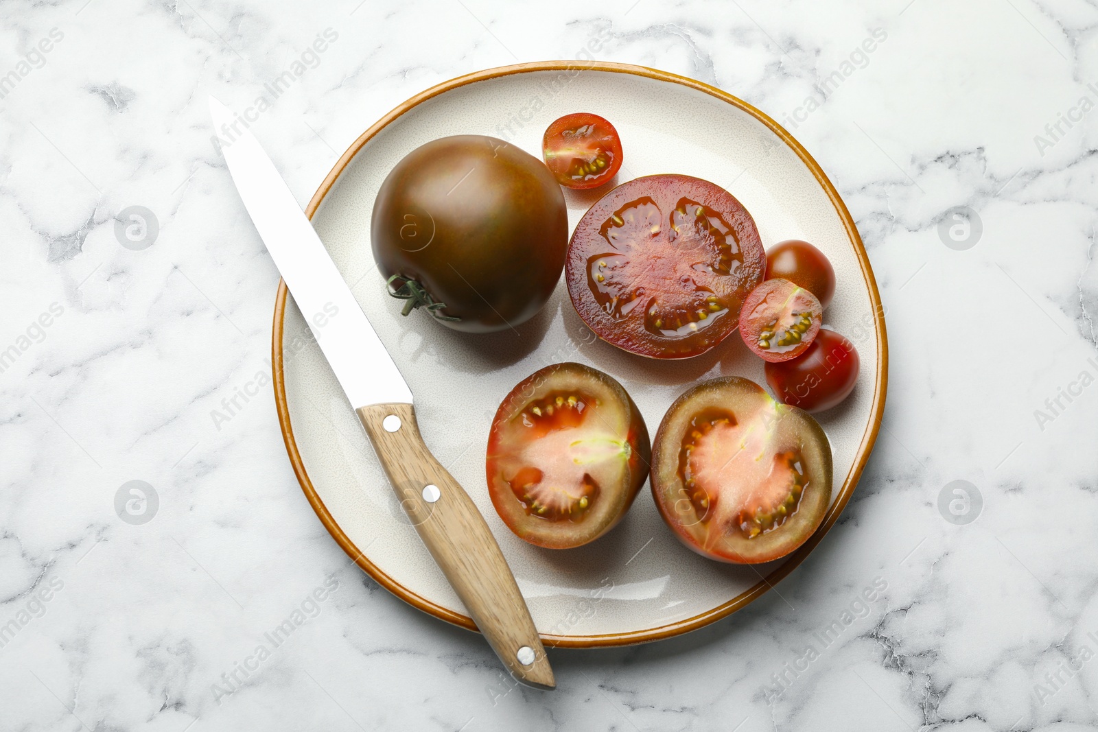 Whole and cut brown tomatoes with knife on white marble table, top view Photo of Whole and cut brown tomatoes with knife on white marble table, top view