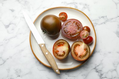 Photo of Whole and cut brown tomatoes with knife on white marble table, top view