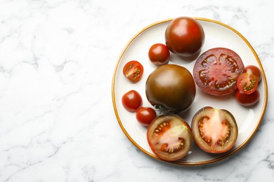 Photo of Whole and cut brown tomatoes on white marble table, top view. Space for text