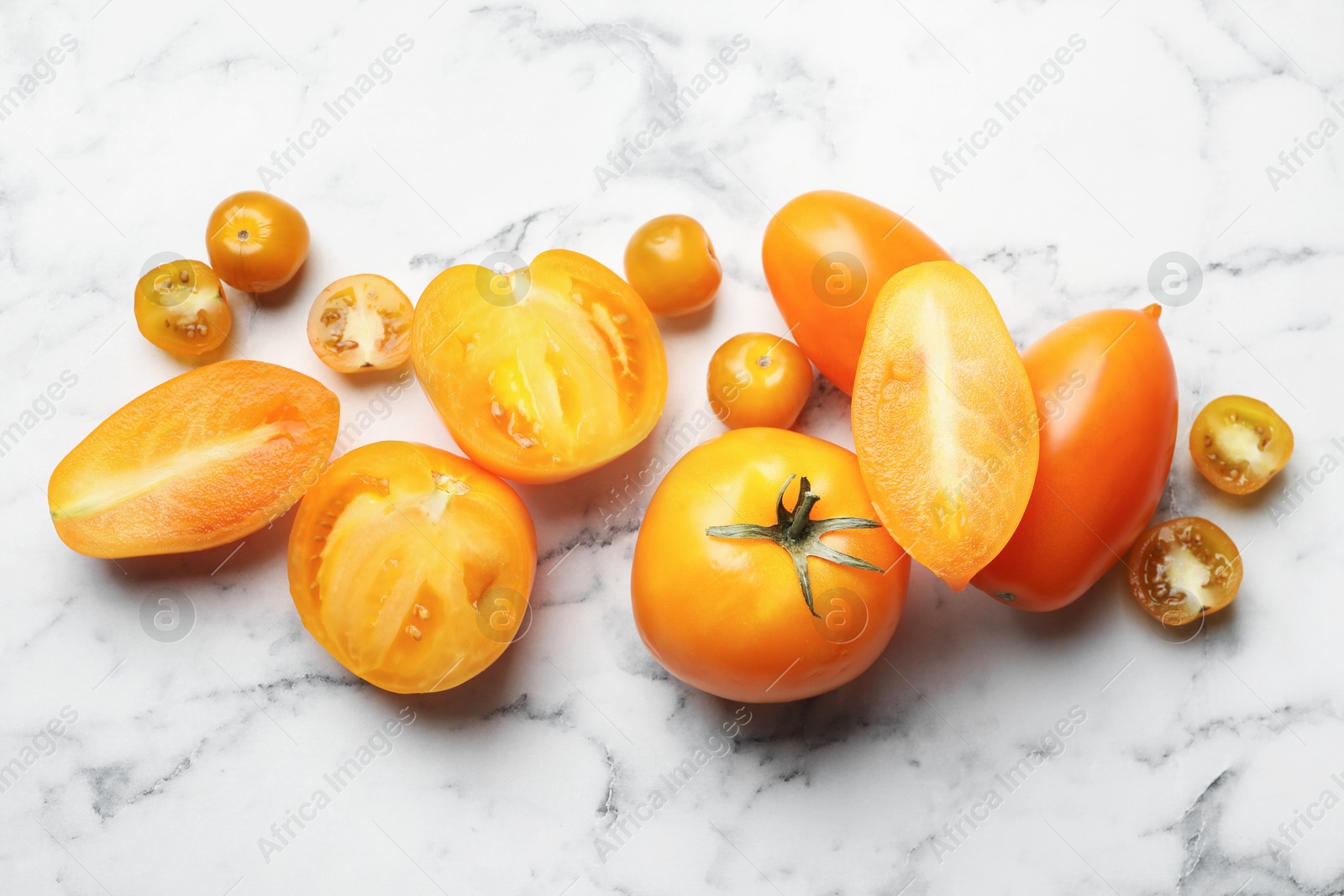 Whole and cut yellow tomatoes on white marble table, flat lay Photo of Whole and cut yellow tomatoes on white marble table, flat lay