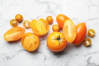 Photo of Whole and cut yellow tomatoes on white marble table, flat lay