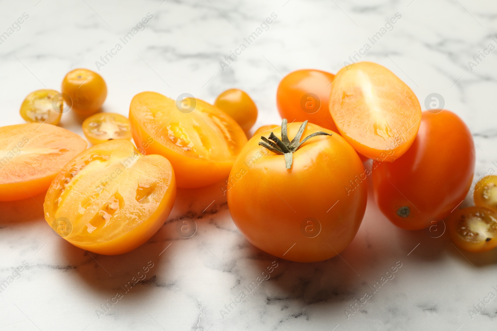 Whole and cut yellow tomatoes on white marble table, closeup Photo of Whole and cut yellow tomatoes on white marble table, closeup