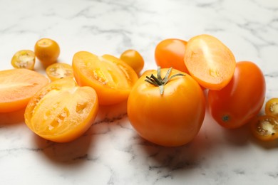 Photo of Whole and cut yellow tomatoes on white marble table, closeup