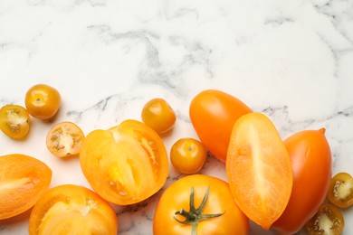 Photo of Whole and cut yellow tomatoes on white marble table, flat lay. Space for text