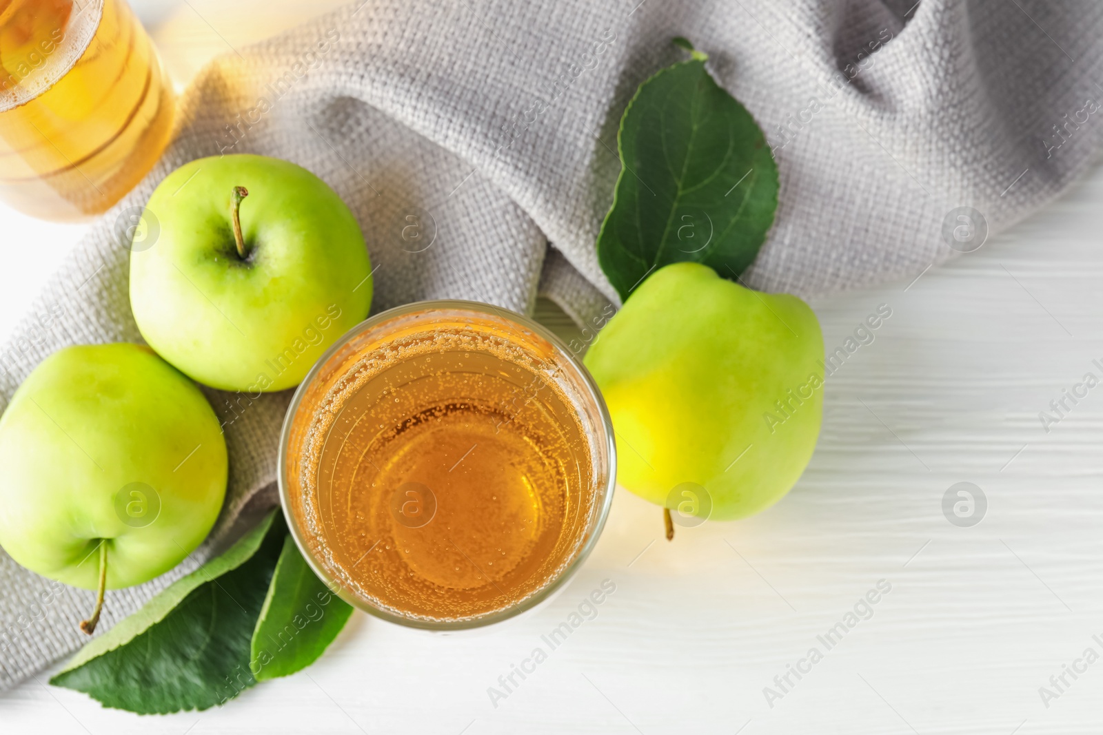 Fresh cider in glass and apples on white wooden table, flat lay Photo of Fresh cider in glass and apples on white wooden table, flat lay