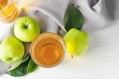Photo of Fresh cider in glass and apples on white wooden table, flat lay