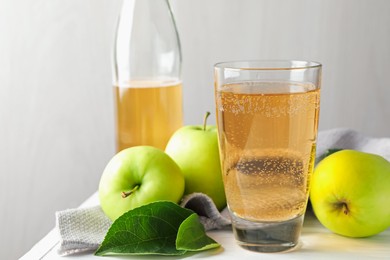 Photo of Fresh cider in glass, bottle and apples on white wooden table, closeup