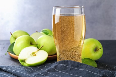 Photo of Fresh cider in glass and apples on black table, closeup