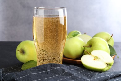 Photo of Fresh cider in glass and apples on black table, closeup