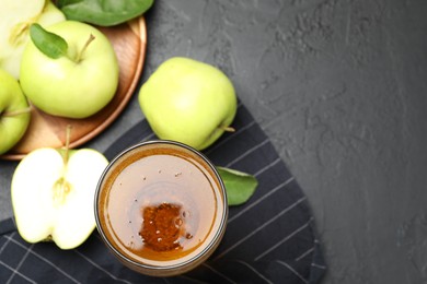 Photo of Fresh cider in glass and apples on black table, flat lay. Space for text
