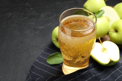Photo of Fresh cider in glass and apples on black table, closeup. Space for text