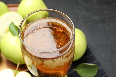 Photo of Fresh cider in glass and apples on black table, closeup