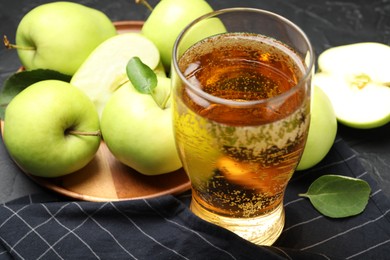 Photo of Fresh cider in glass and apples on black table, closeup