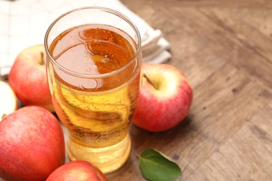 Photo of Fresh cider in glass and apples on wooden table, closeup. Space for text