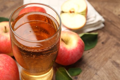 Photo of Fresh cider in glass and apples on wooden table, closeup. Space for text