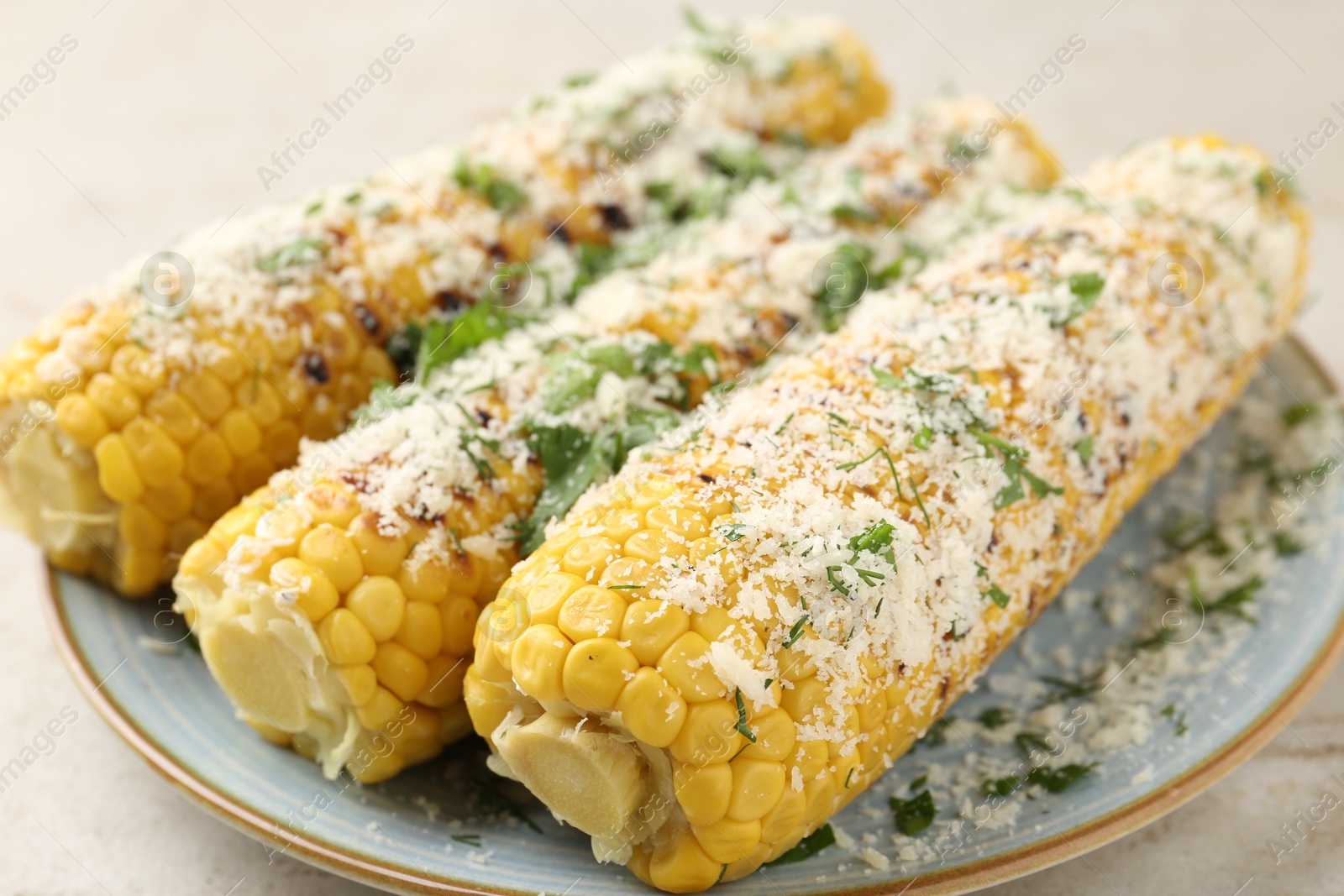 Photo of Tasty grilled corncobs with parsley and cheese on light table, closeup