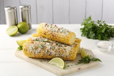 Photo of Tasty grilled corncobs with parsley, cheese and lime slices on white wooden table