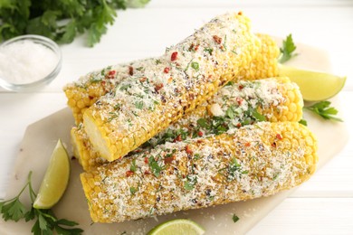 Photo of Tasty grilled corncobs with parsley, cheese and lime slices on white wooden table, closeup