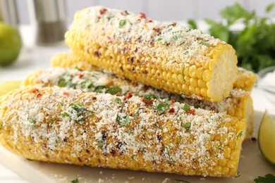 Photo of Tasty grilled corncobs with parsley and cheese on white table, closeup