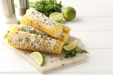 Photo of Tasty grilled corncobs with parsley, cheese and lime slices on white wooden table