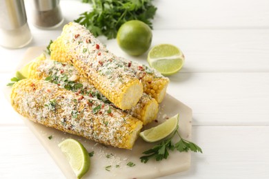 Photo of Tasty grilled corncobs with parsley, cheese and lime slices on white wooden table