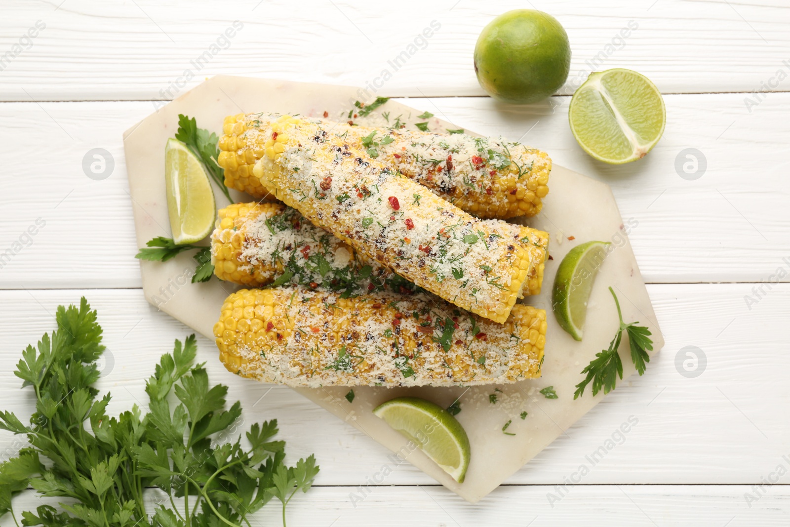 Photo of Tasty grilled corncobs with parsley, cheese and lime slices on white wooden table, flat lay