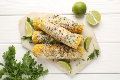 Photo of Tasty grilled corncobs with parsley, cheese and lime slices on white wooden table, flat lay