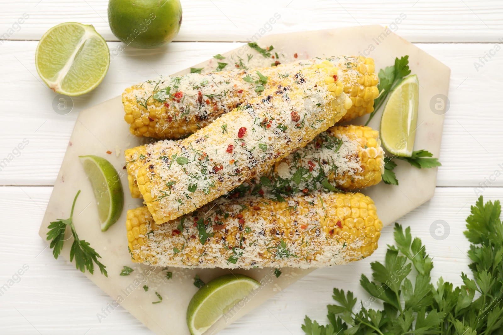 Photo of Tasty grilled corncobs with parsley, cheese and lime slices on white wooden table, flat lay