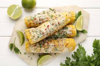 Photo of Tasty grilled corncobs with parsley, cheese and lime slices on white wooden table, flat lay