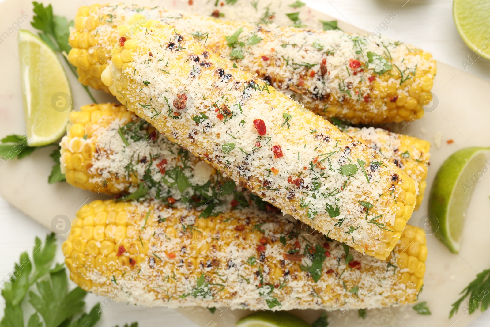Photo of Tasty grilled corncobs with parsley, cheese and lime slices on white wooden table, flat lay
