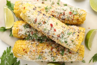 Photo of Tasty grilled corncobs with parsley, cheese and lime slices on white wooden table, flat lay