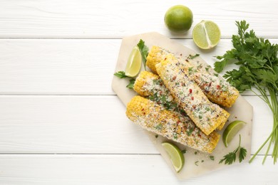 Photo of Tasty grilled corncobs with parsley, cheese and lime slices on white wooden table, flat lay. Space for text