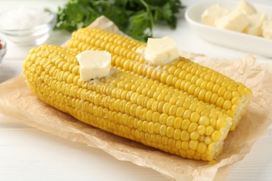 Photo of Tasty boiled corncobs with butter on white wooden table, closeup