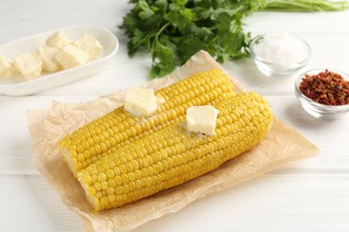 Photo of Tasty boiled corncobs with butter, spices and parsley on white wooden table, closeup