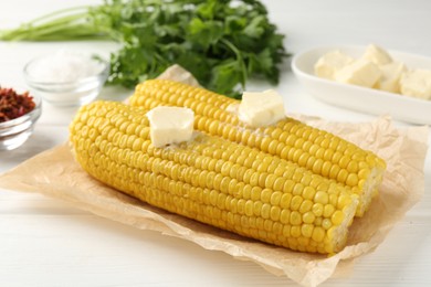 Photo of Tasty boiled corncobs with butter, spices and parsley on white wooden table, closeup