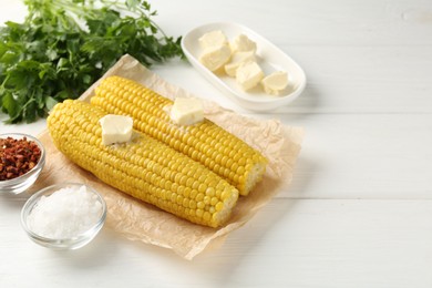 Photo of Tasty boiled corncobs with butter, spices and parsley on white wooden table