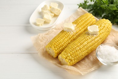 Photo of Tasty boiled corncobs with butter, salt and parsley on white wooden table