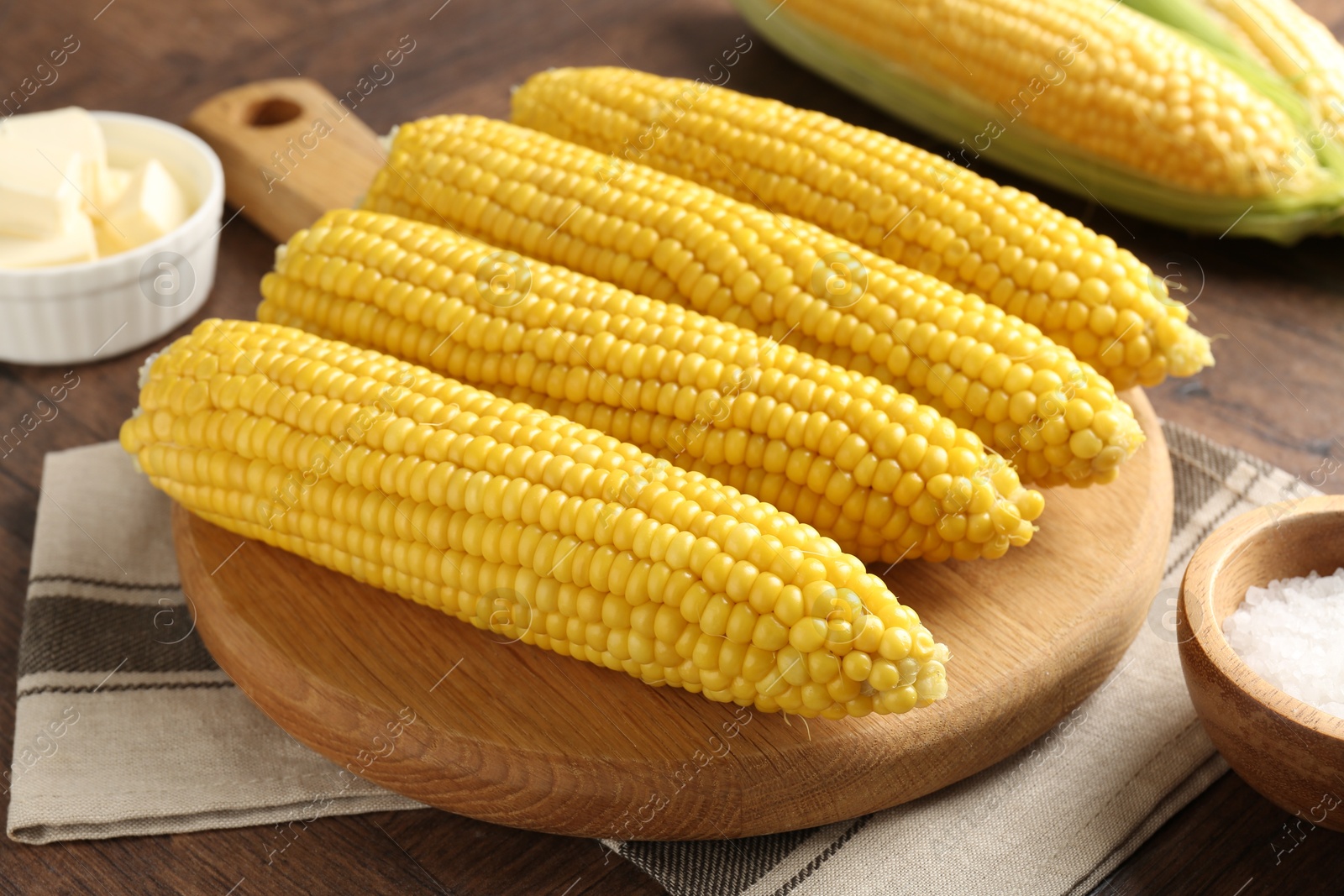 Tasty boiled corncobs, salt and butter on wooden table, closeup Photo of Tasty boiled corncobs, salt and butter on wooden table, closeup