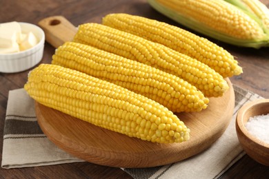 Photo of Tasty boiled corncobs, salt and butter on wooden table, closeup
