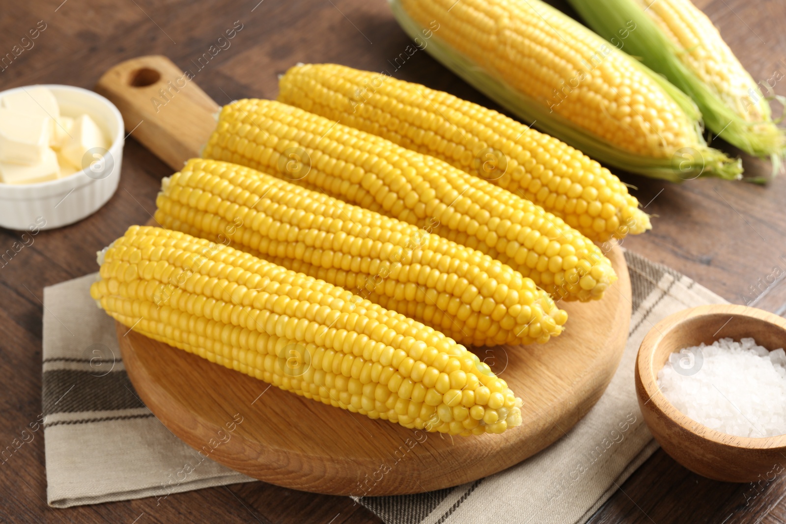 Tasty boiled corncobs, salt and butter on wooden table, closeup Photo of Tasty boiled corncobs, salt and butter on wooden table, closeup