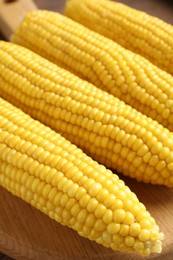 Photo of Tasty boiled corncobs on wooden table, closeup