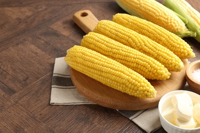 Photo of Tasty boiled corncobs and butter on wooden table, closeup